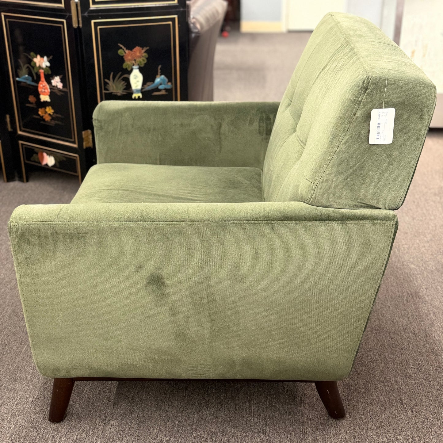 Green armchair with a tag on a gray carpeted floor