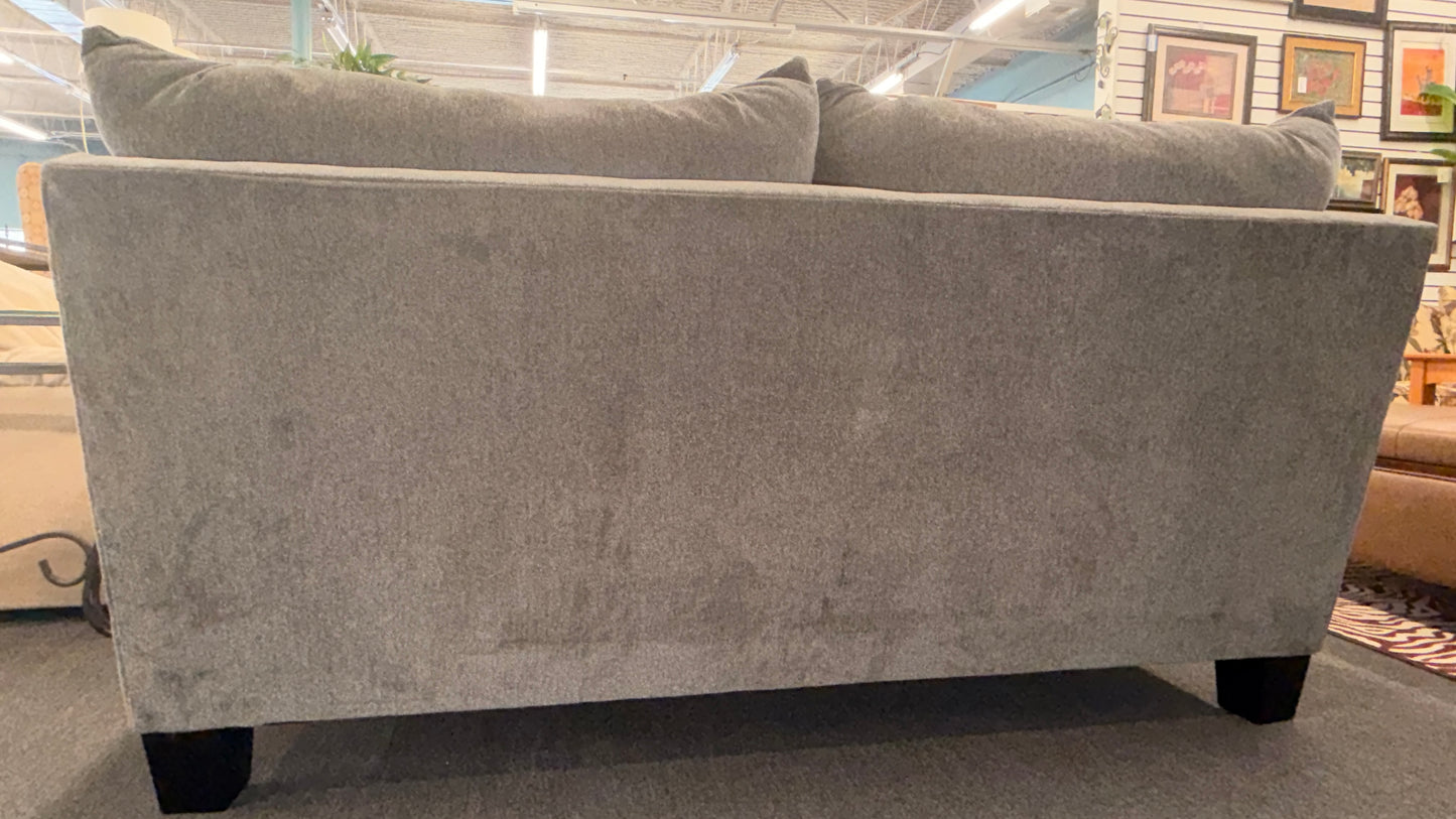 Gray sofa in a store setting with framed pictures on the wall.