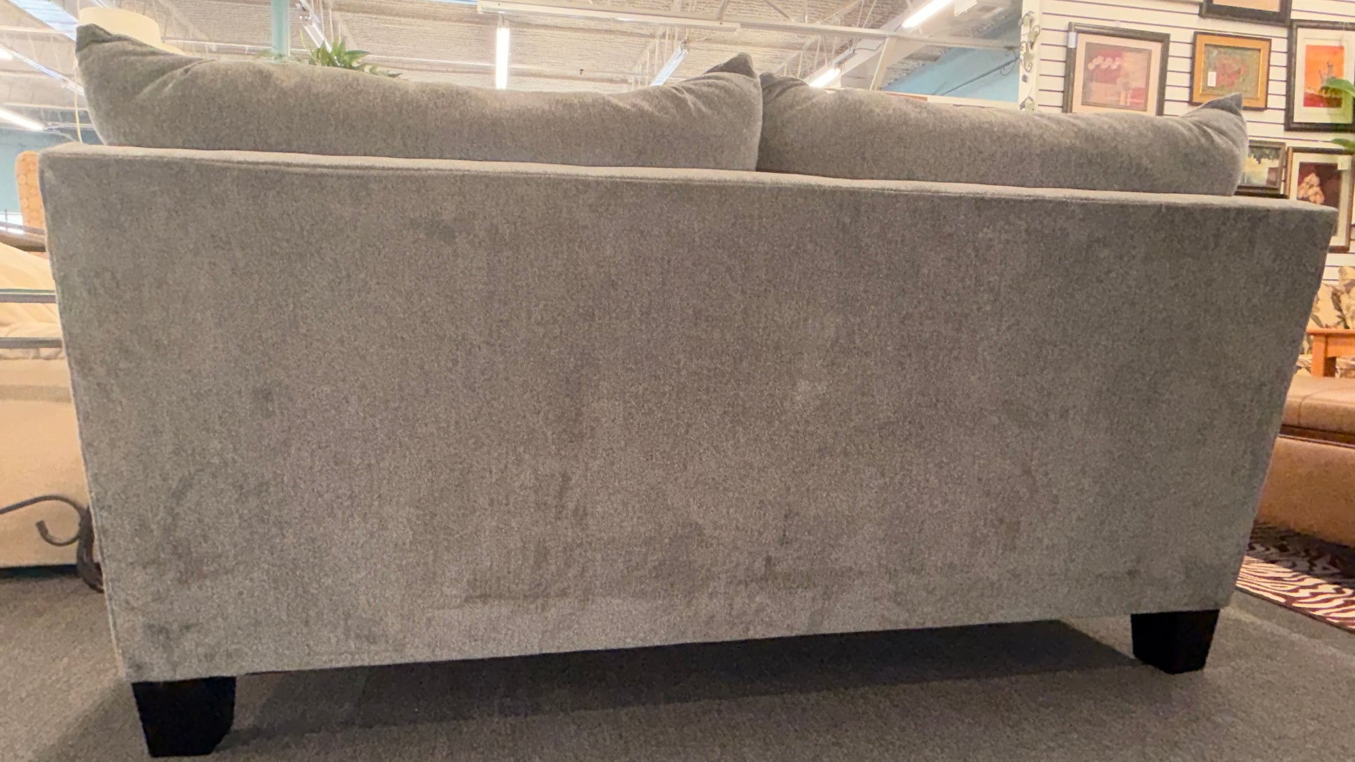 Gray sofa in a store setting with framed pictures on the wall.