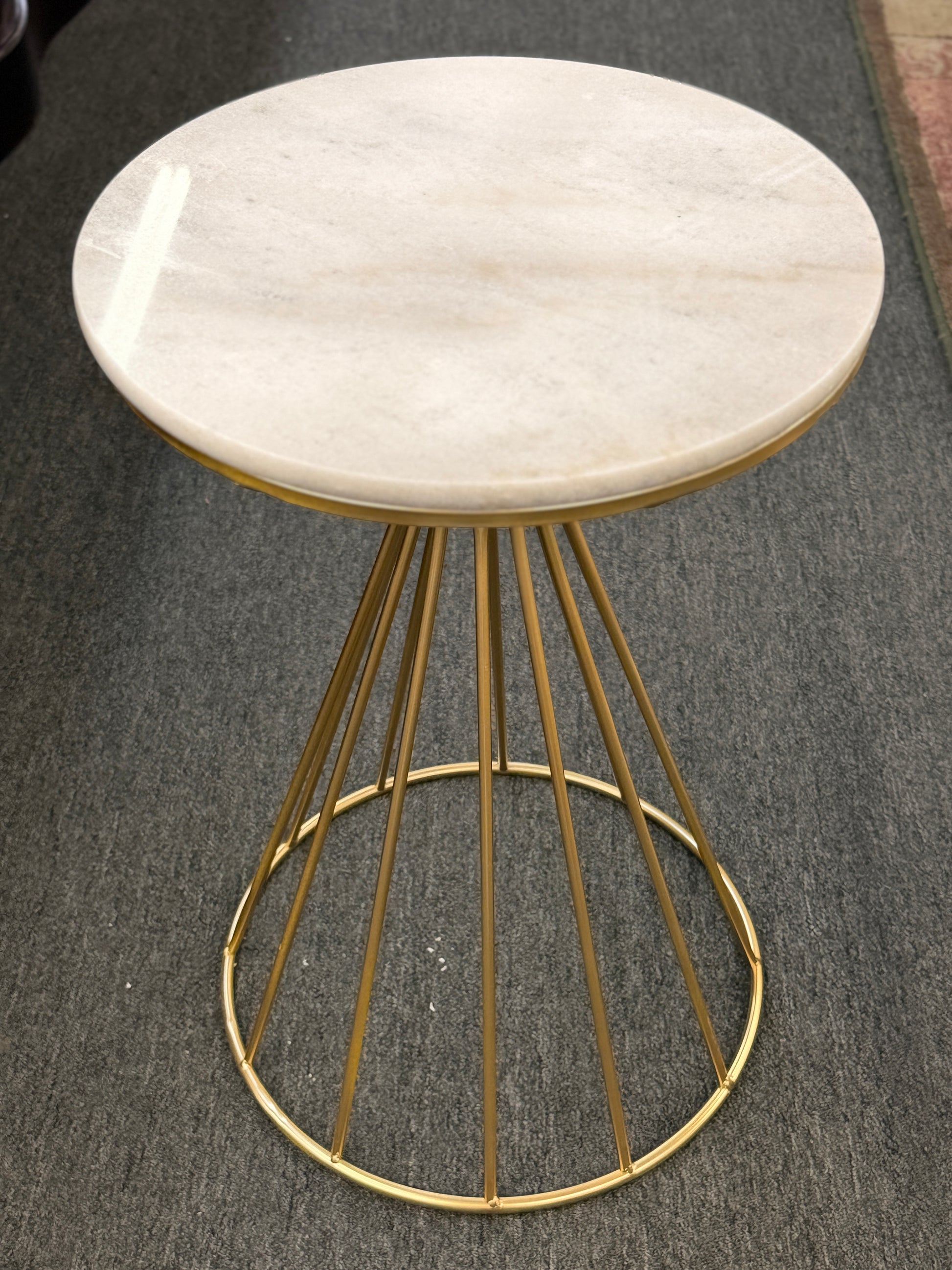 Small round table with marble top and gold metal base on a gray floor.