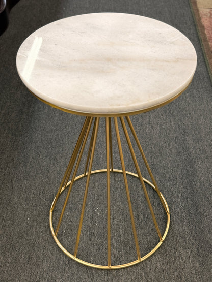 Small round table with marble top and gold metal base on a gray floor.