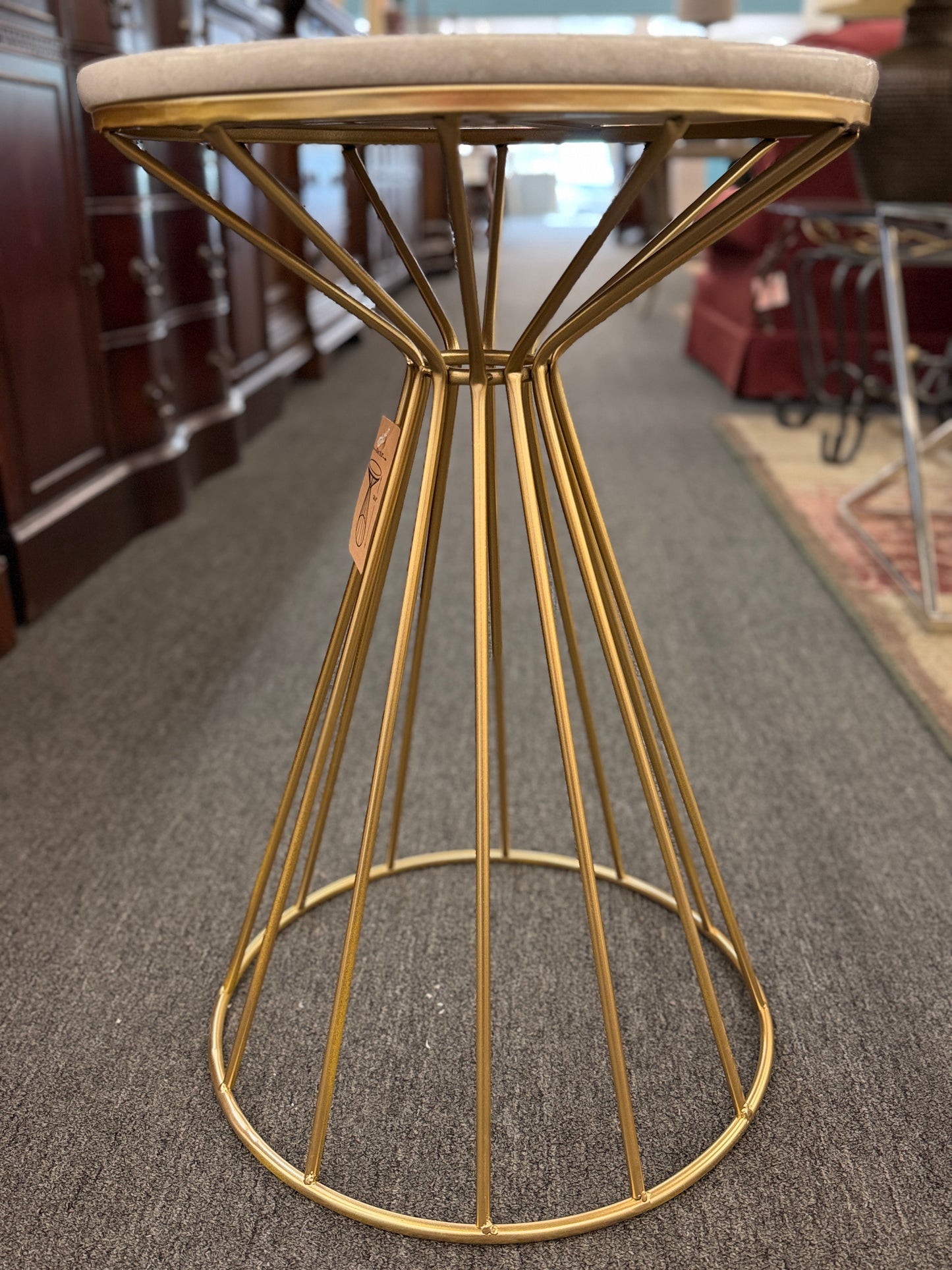 Gold wireframe stool with a beige cushioned seat on a carpeted floor.