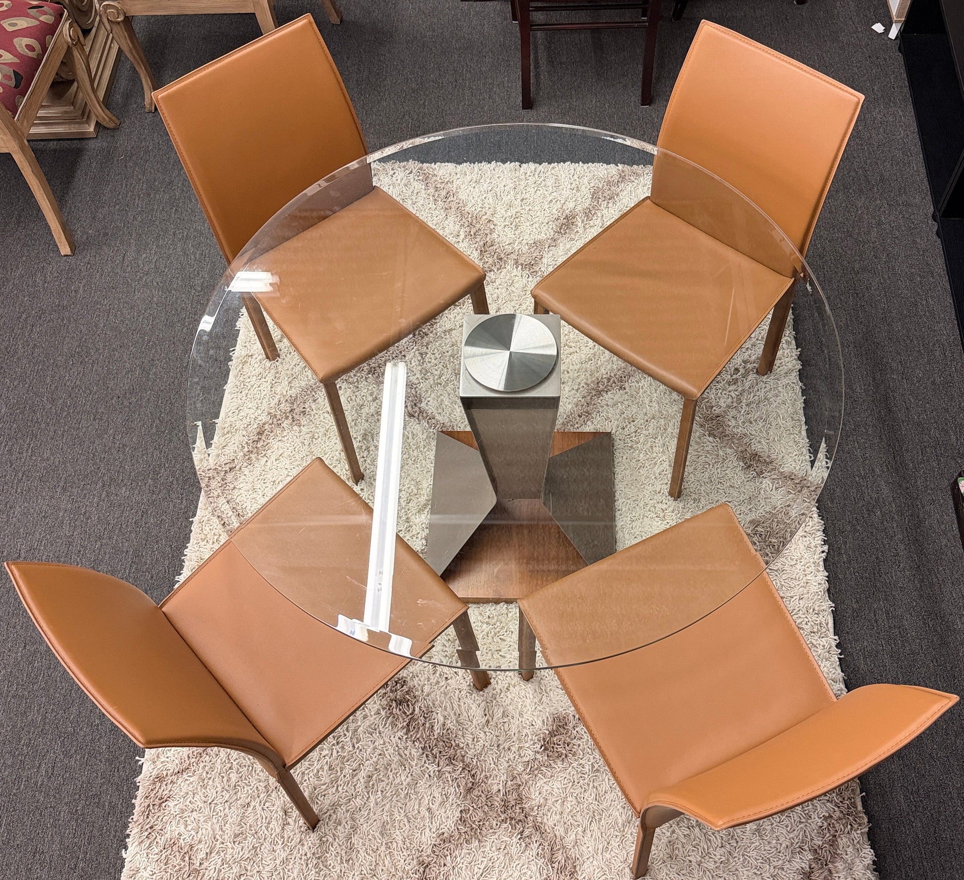 Four brown chairs around a glass dining table on a textured rug.