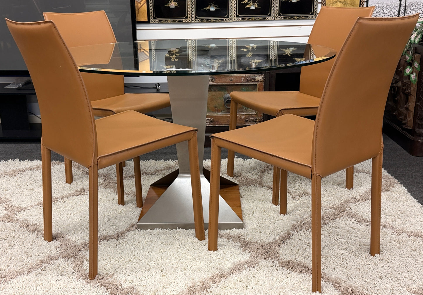 Dining table with four brown chairs on a textured white rug.