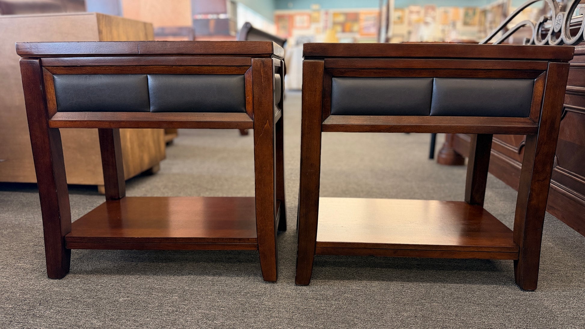 Two wooden side tables with leather seats in a showroom setting.