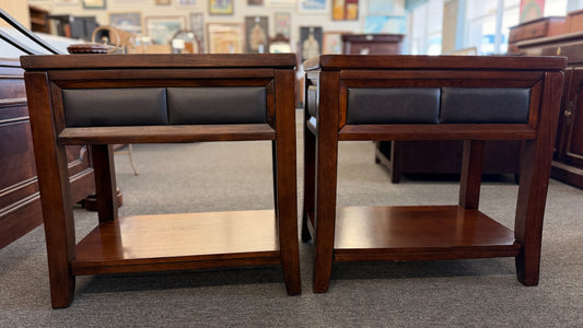 Two wooden side tables with leather seats in a showroom setting.