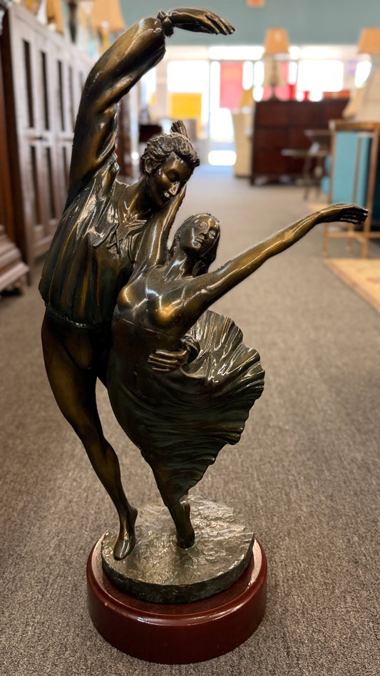 Bronze sculpture of two dancers on a wooden base in a store setting