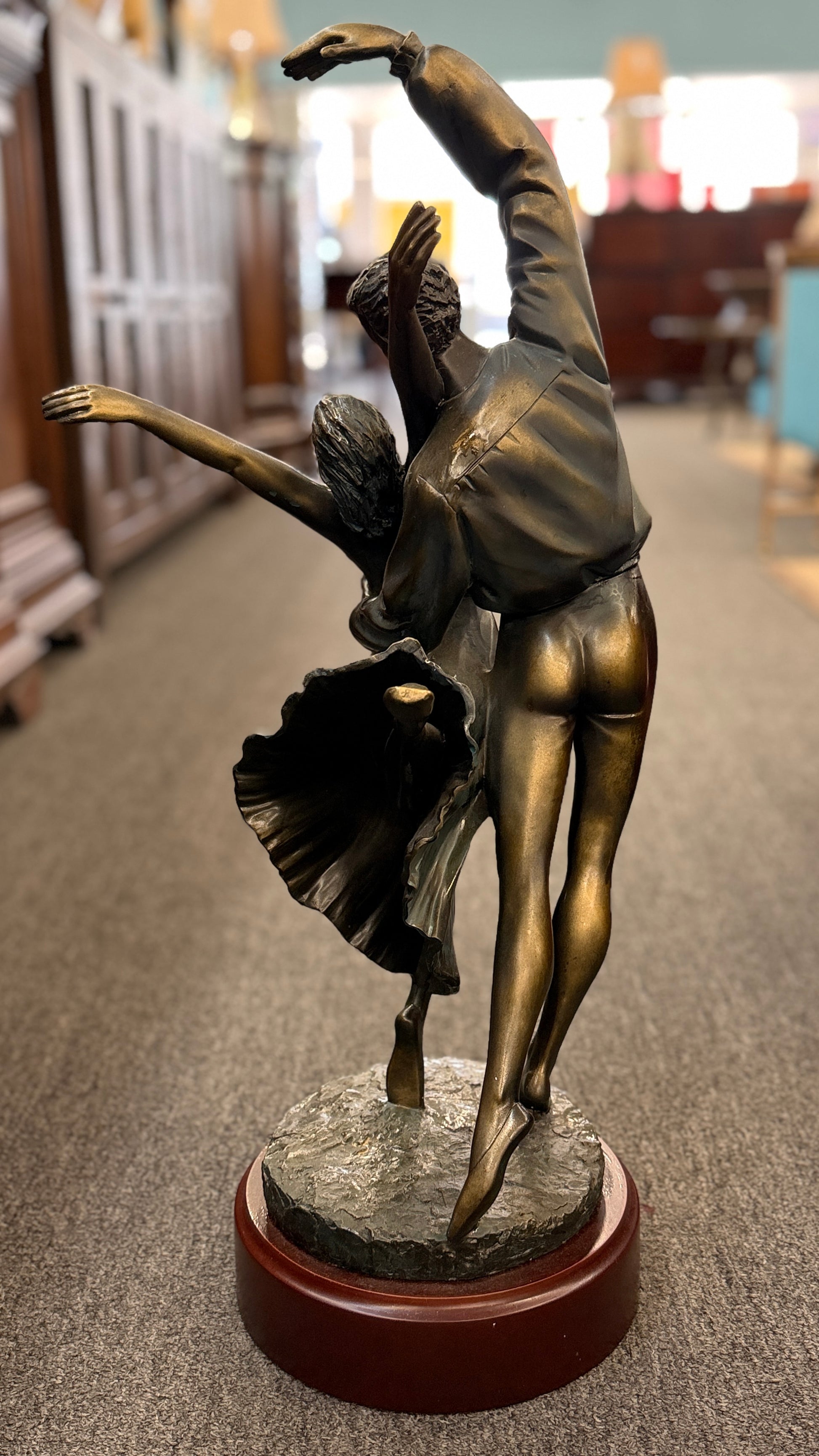Bronze sculpture of two dancers on a wooden base in a store setting