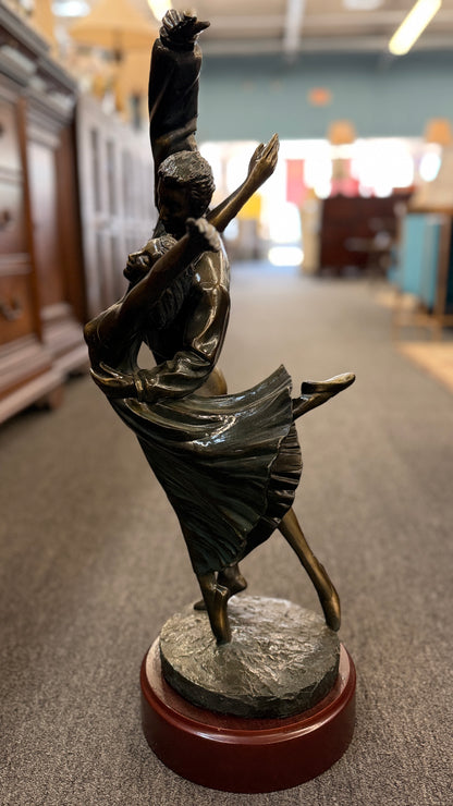 Bronze sculpture of two dancers on a wooden base in a store setting