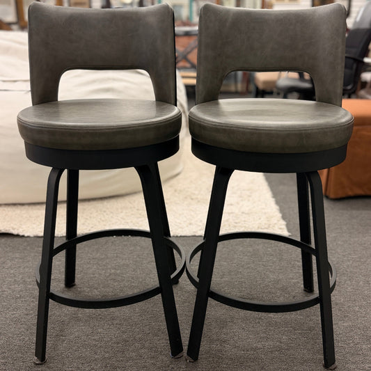 Two gray cushioned bar stools with black metal legs on a carpeted floor.