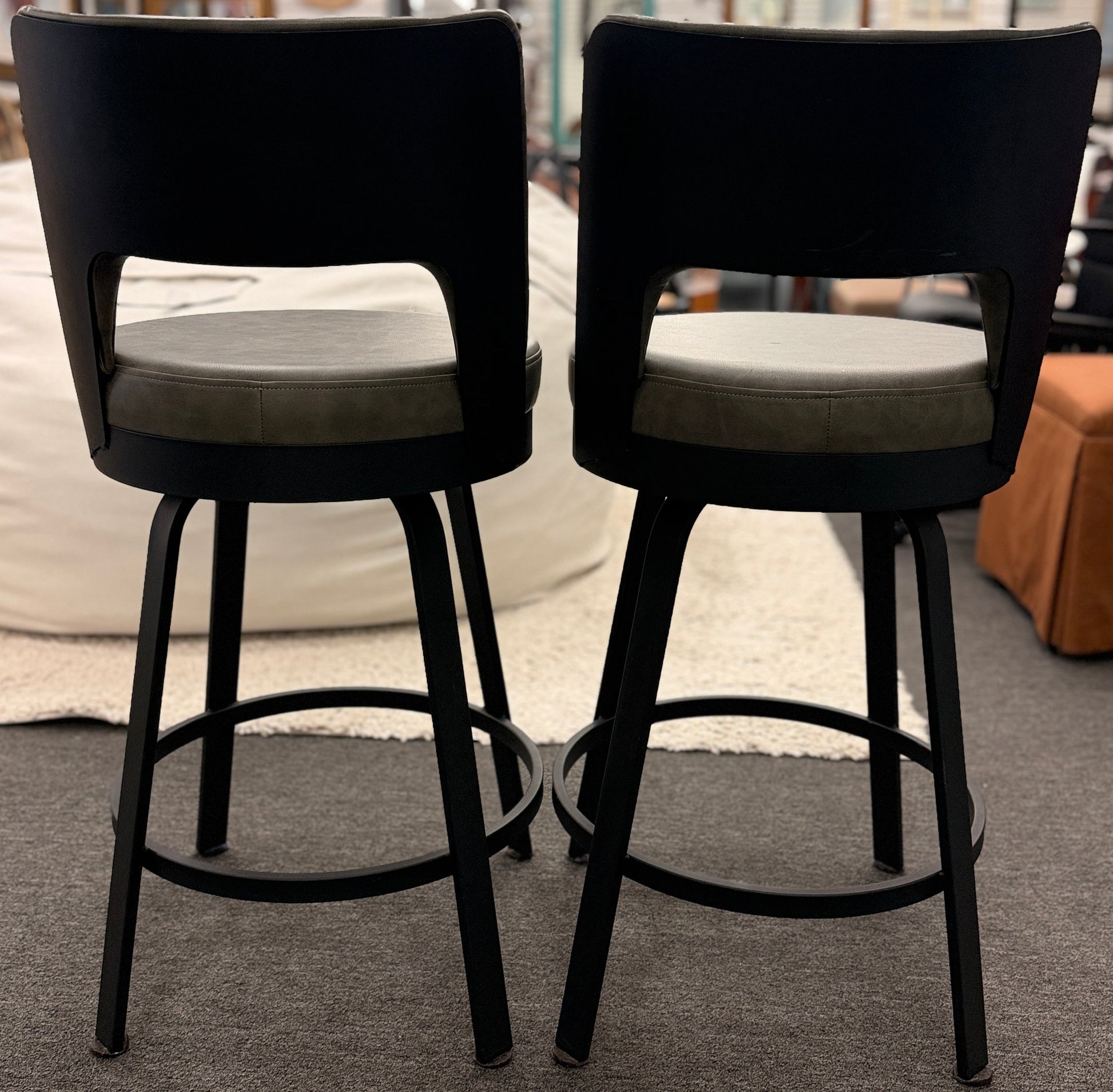 Two black bar stools with gray cushions on a carpeted floor.
