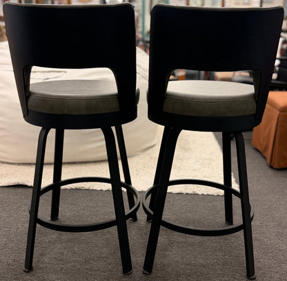 Two black bar stools with gray cushions on a carpeted floor.