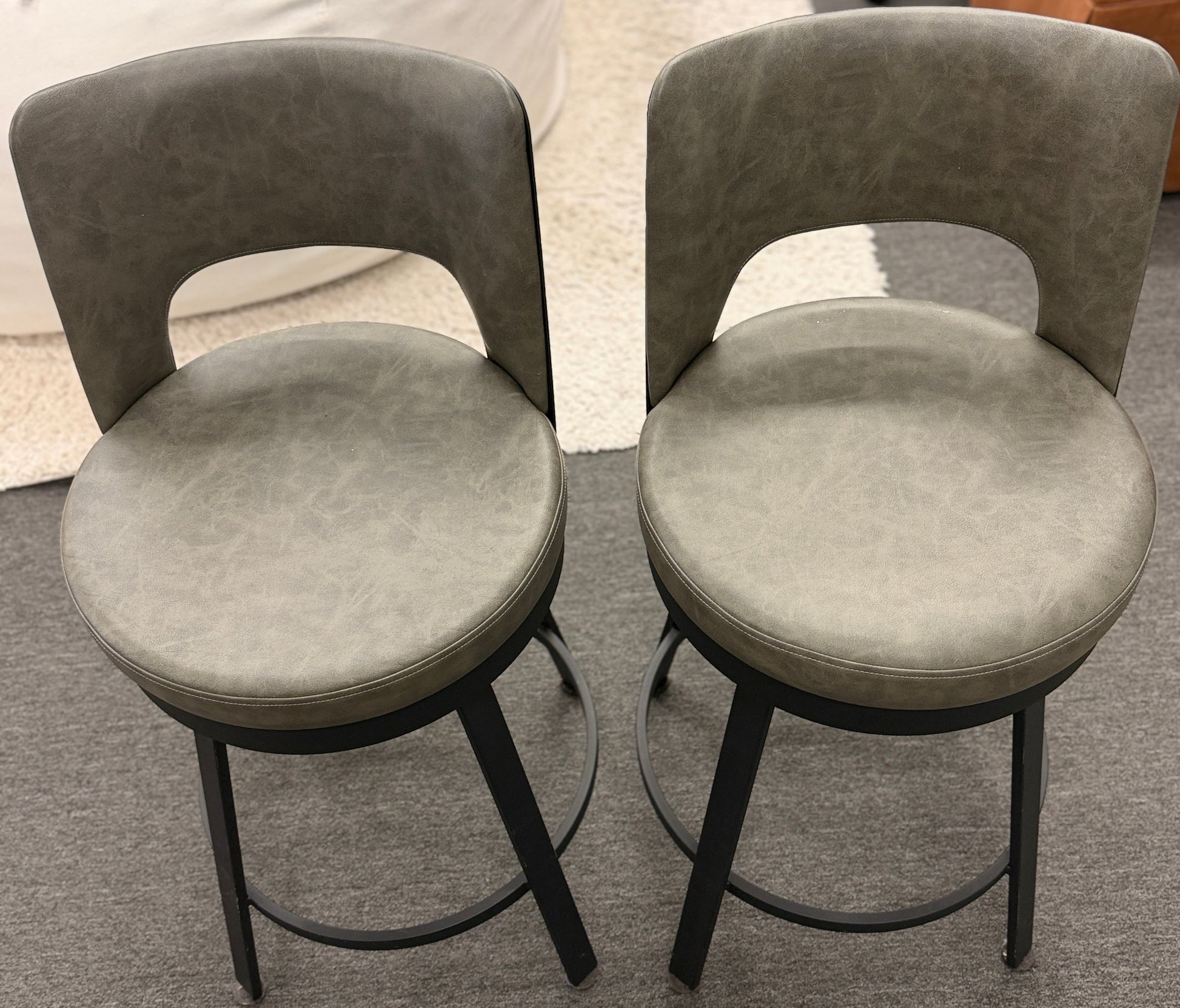 Two gray cushioned stools with black metal legs on a gray floor.