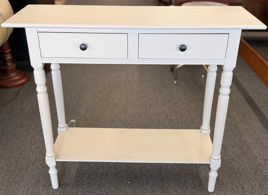 White console table with two drawers and a shelf on a carpeted floor.