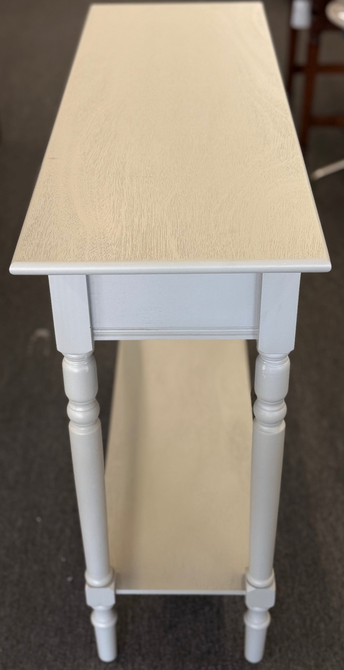Tall narrow table with a light wooden top and white legs on a carpeted floor.