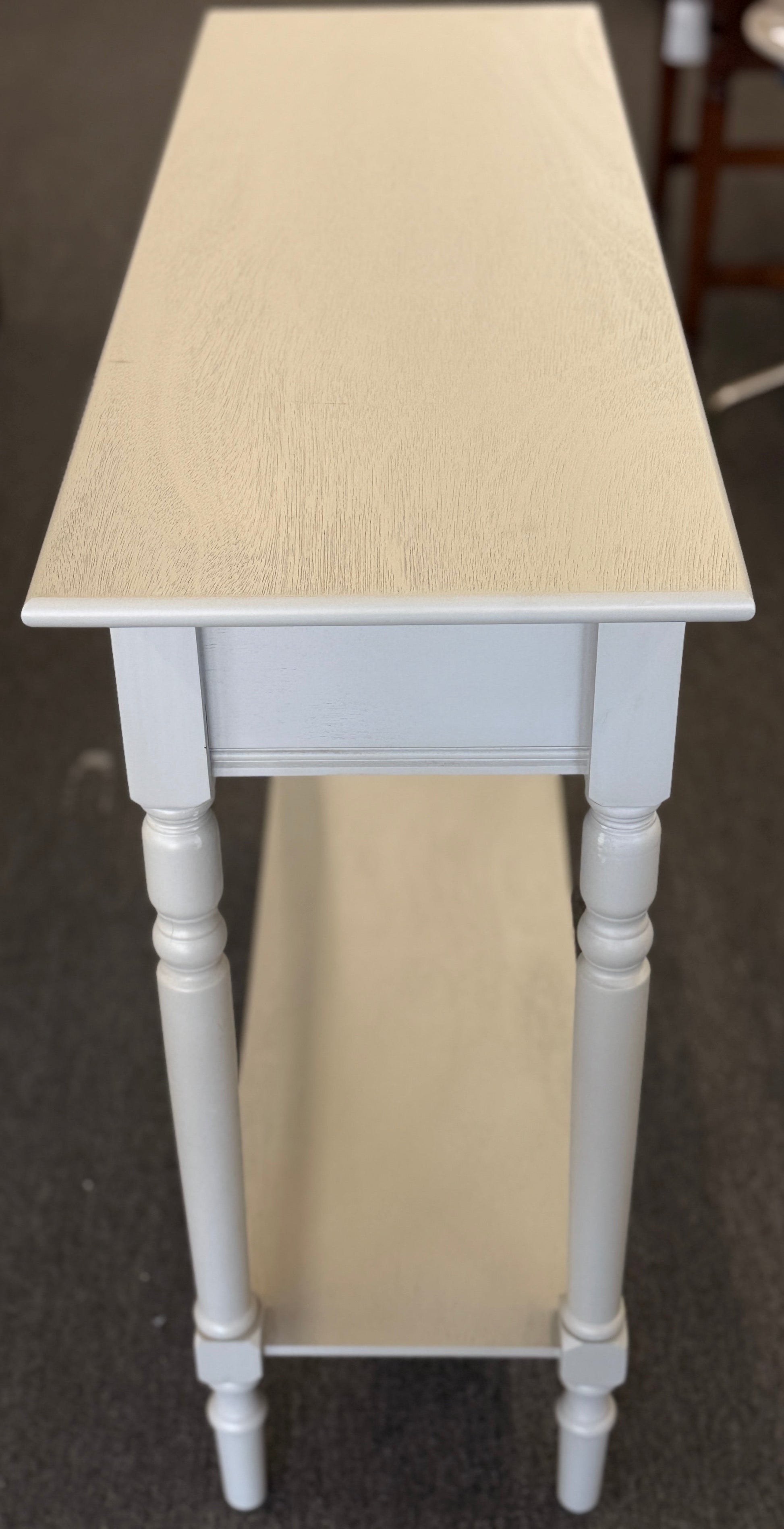 Tall narrow table with a light wooden top and white legs on a carpeted floor.