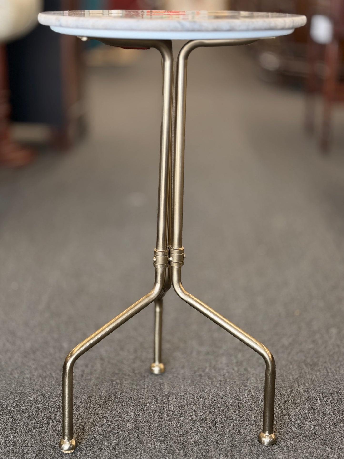Small round table with marble top and brass legs on a gray floor.