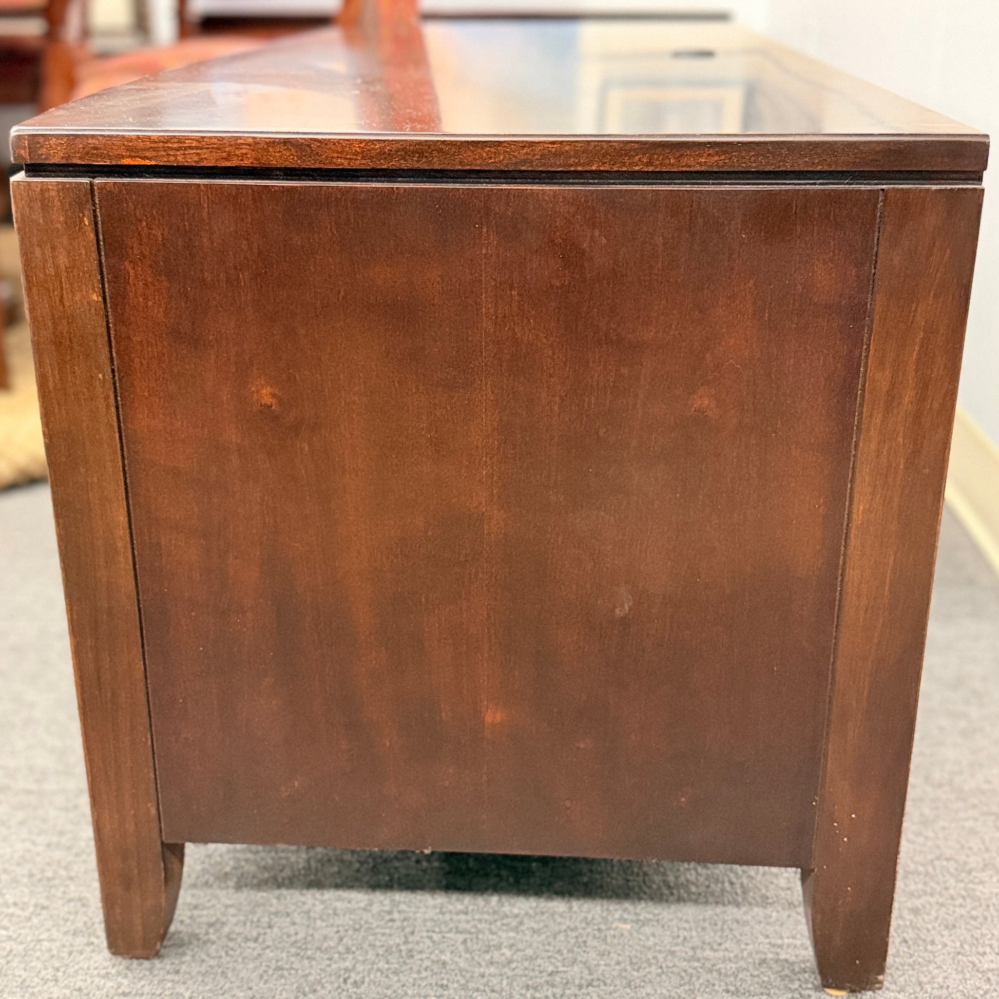 Wooden side table with glass top on a gray floor