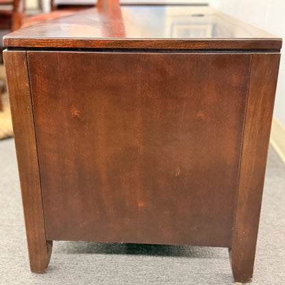 Wooden side table with glass top on a gray floor