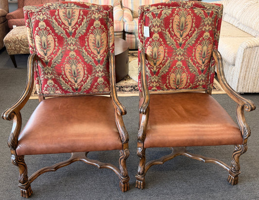 Pair of ornate chairs with red patterned backs and brown leather seats in a room setting.