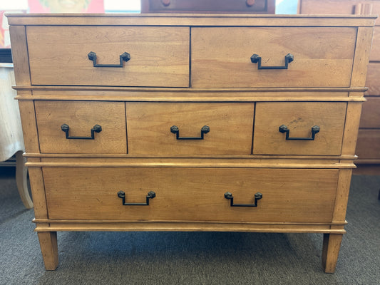 Wooden dresser with multiple drawers and handles in a room setting.