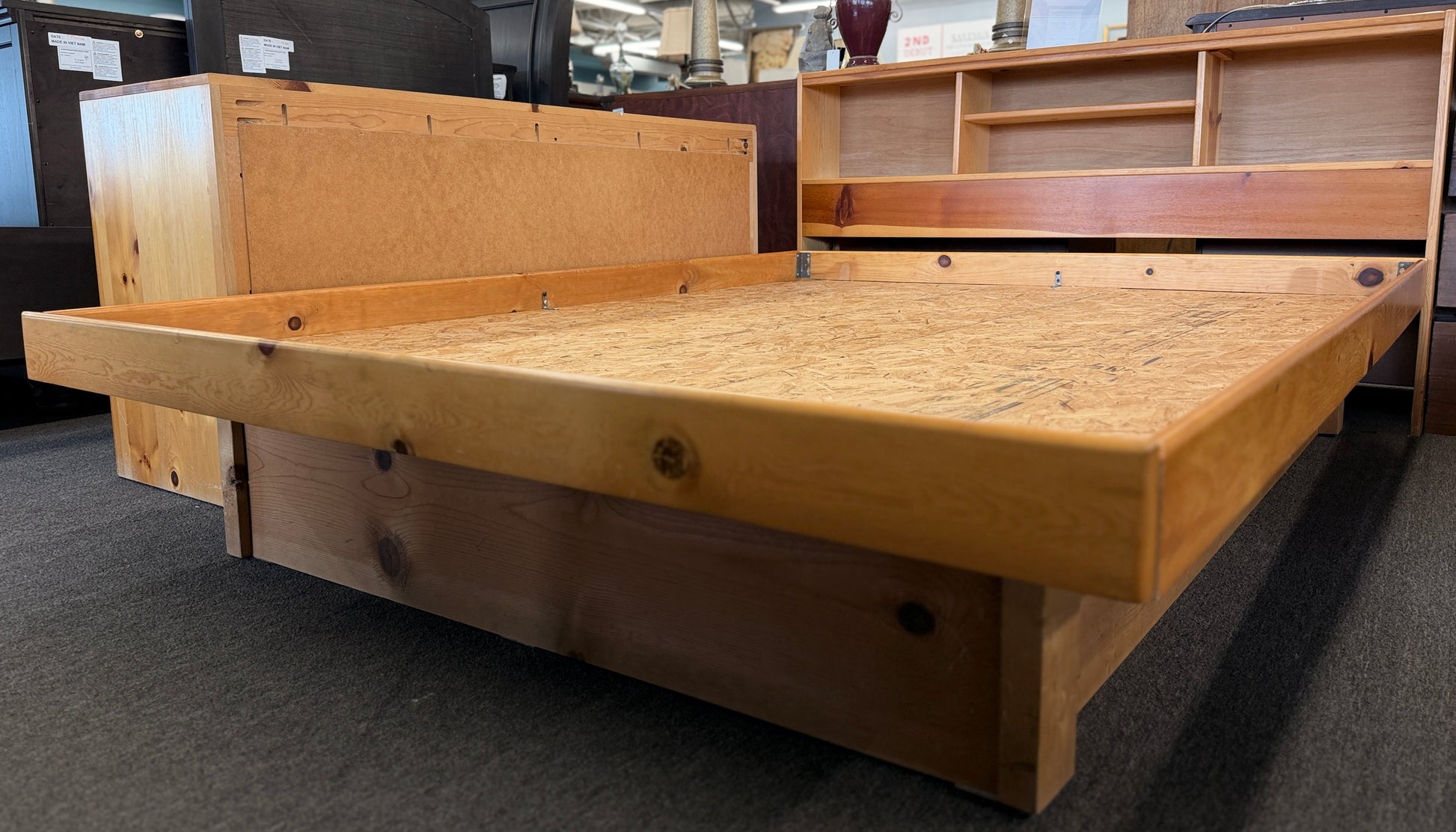 Wooden bed frame in a store setting with other furniture items.