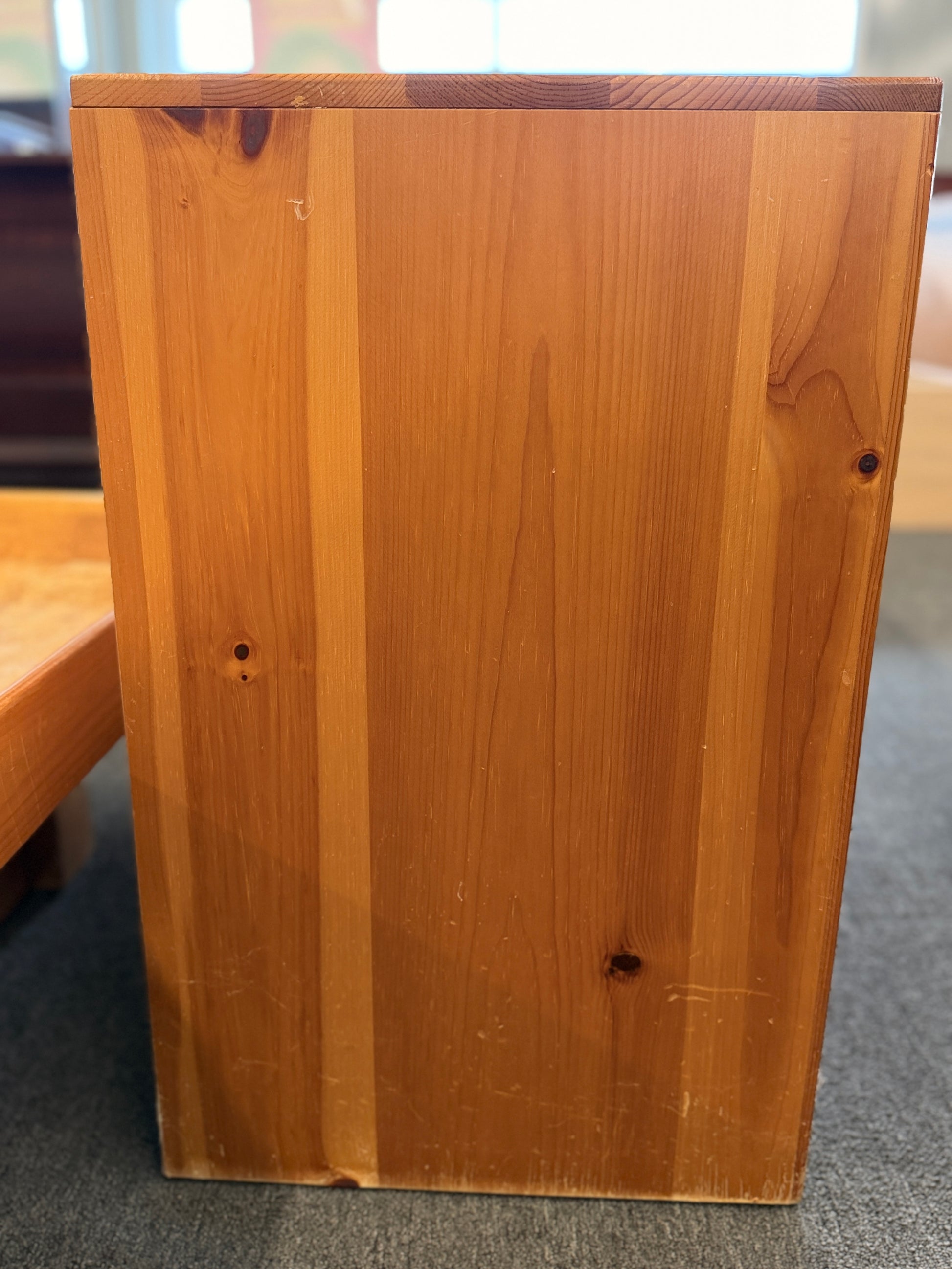 Wooden box with a visible grain pattern on a carpeted floor.