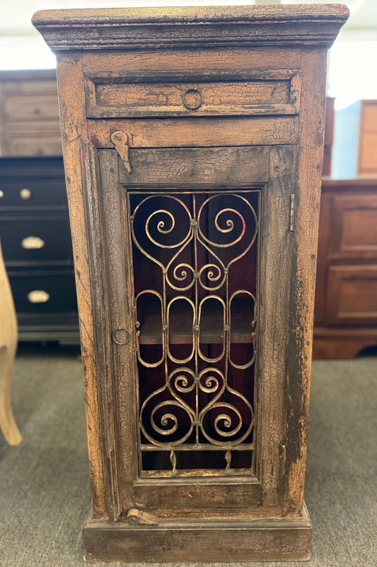 Wooden cabinet with decorative metal grille in a room with other furniture.