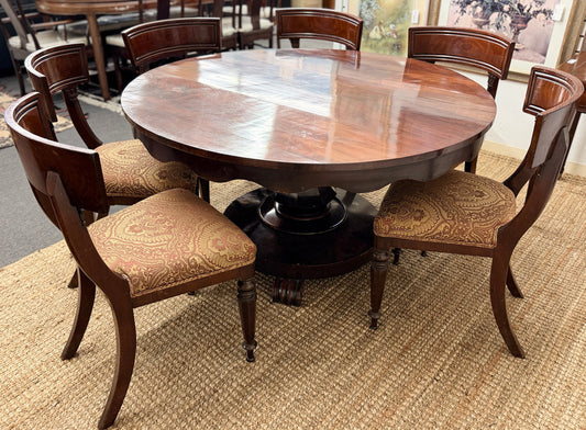 Round wooden dining table with six matching chairs in a room setting.