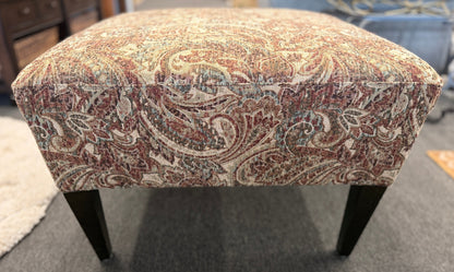 Patterned ottoman on a carpeted floor with furniture in the background