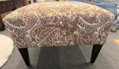 Patterned ottoman on a carpeted floor with furniture in the background
