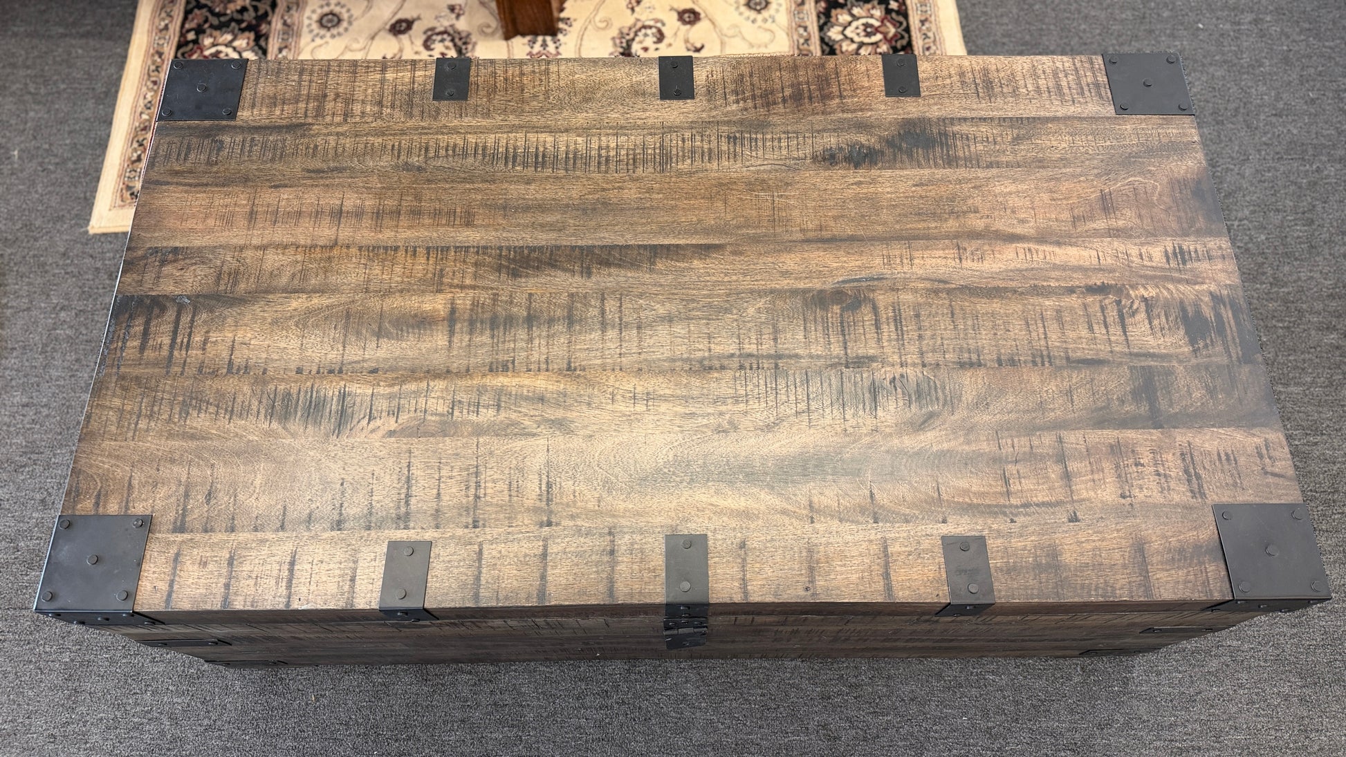 A rustic industrial trunk coffee table made of distressed dark wood with black iron corner brackets, open partially to reveal a lift-top mechanism and internal storage space.