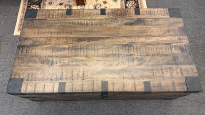 A rustic industrial trunk coffee table made of distressed dark wood with black iron corner brackets, open partially to reveal a lift-top mechanism and internal storage space.