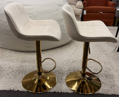 A pair of modern swivel bar stools featuring low-profile upholstered seats with vertical channel tufting on gleaming metallic pedestal bases with footrests.