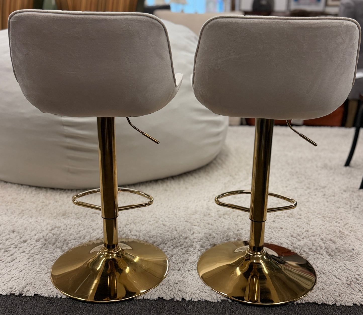 A pair of modern swivel bar stools featuring low-profile upholstered seats with vertical channel tufting on gleaming metallic pedestal bases with footrests.