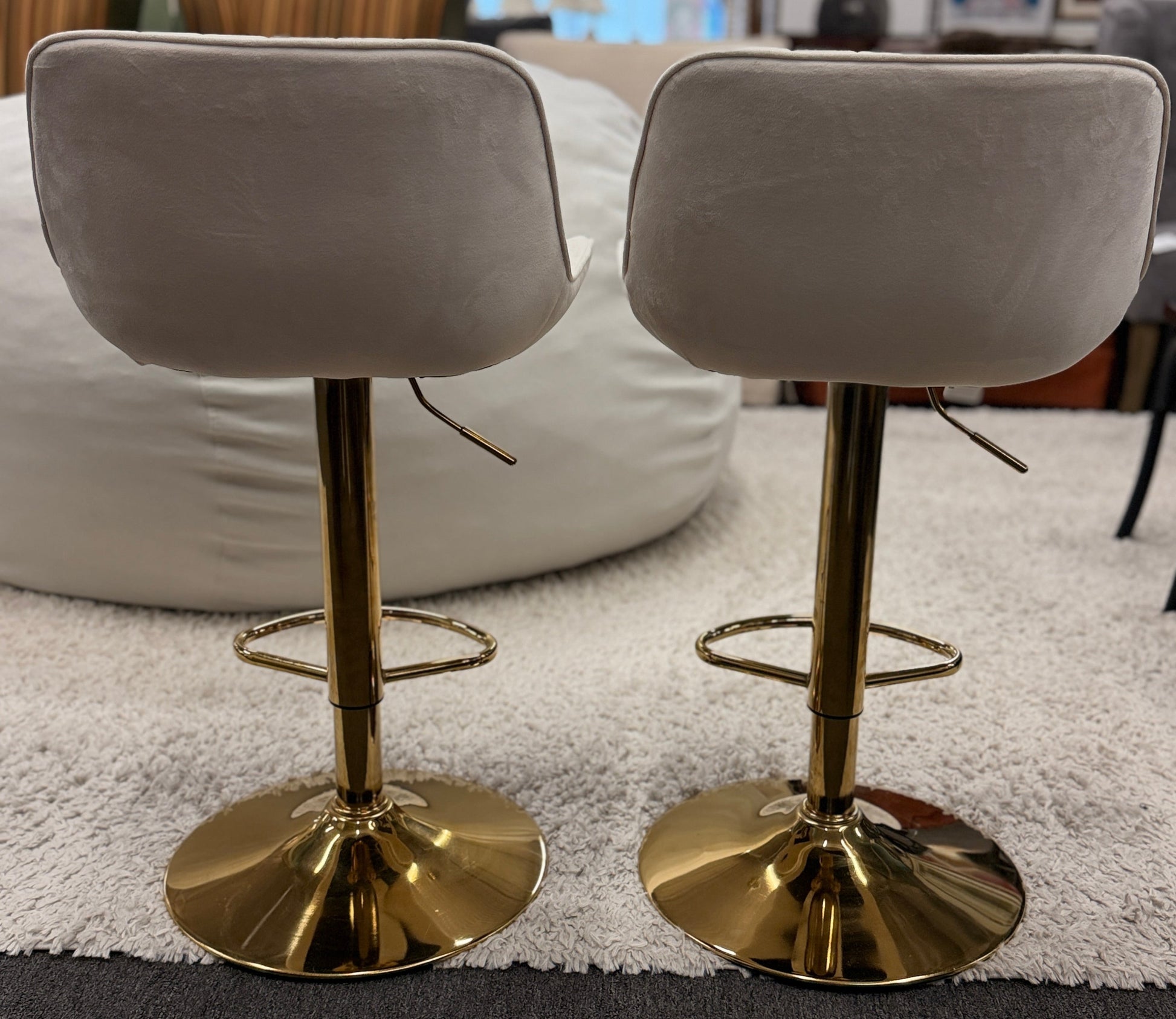 A pair of modern swivel bar stools featuring low-profile upholstered seats with vertical channel tufting on gleaming metallic pedestal bases with footrests.