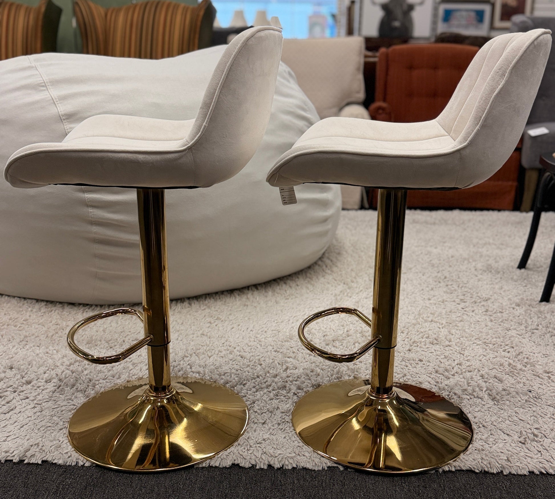 A pair of modern swivel bar stools featuring low-profile upholstered seats with vertical channel tufting on gleaming metallic pedestal bases with footrests.