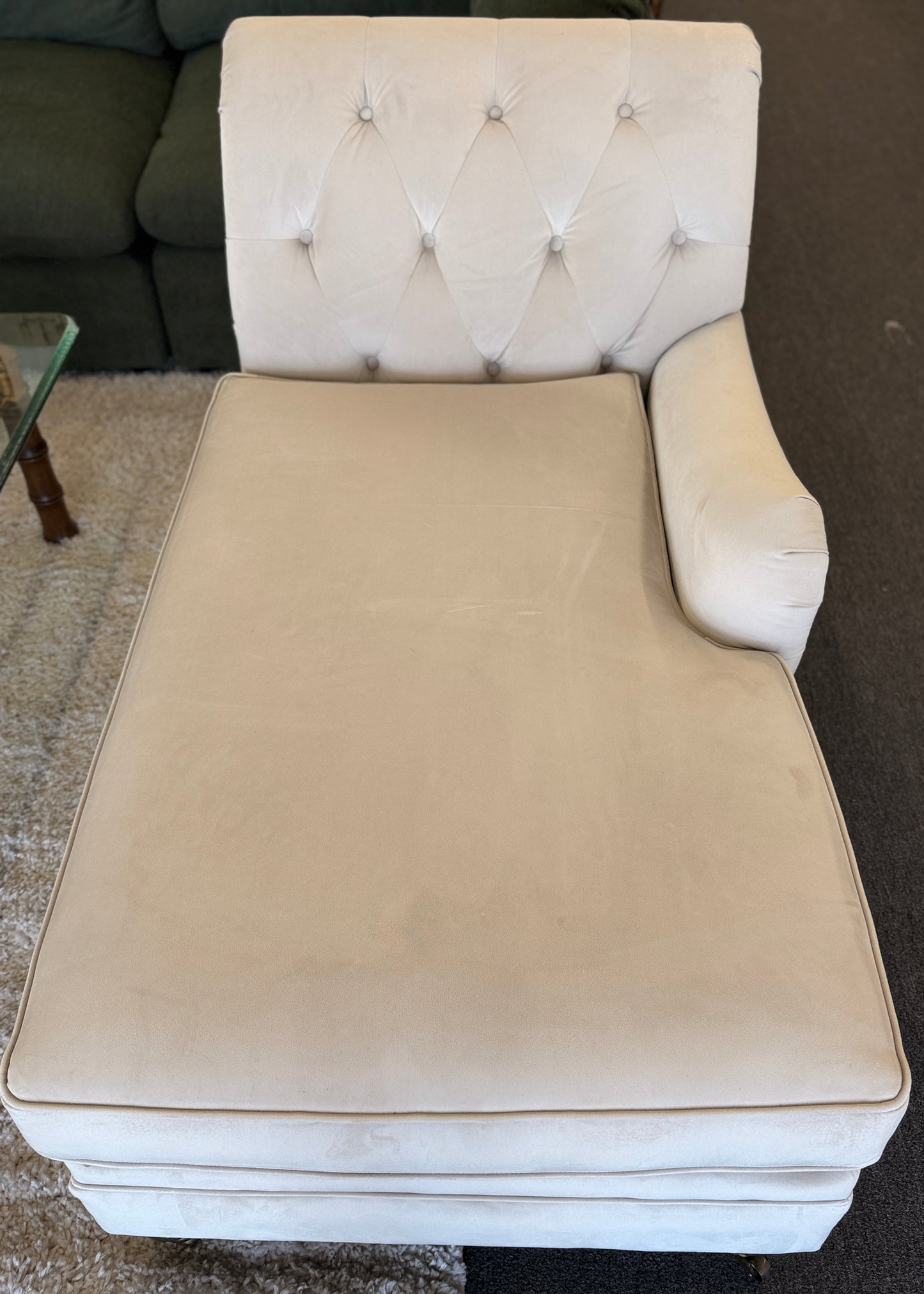 A vintage-style Bassett chaise lounge with a tufted rolled backrest, plush fabric cushion, and turned wooden legs on front casters.
