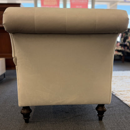A vintage-style Bassett chaise lounge with a tufted rolled backrest, plush fabric cushion, and turned wooden legs on front casters.