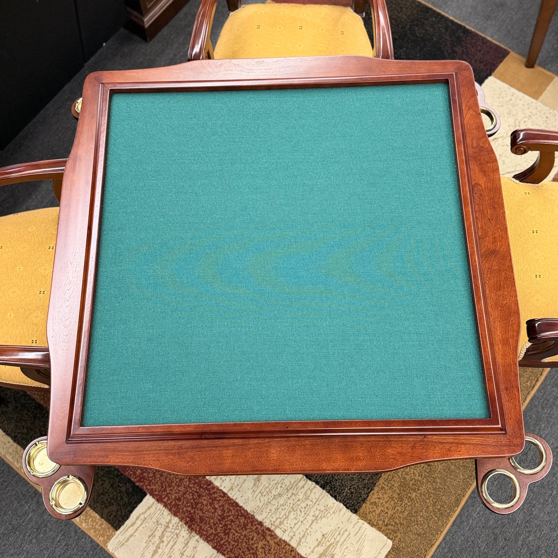 A 5-piece traditional game table set featuring a square wood table with a green felt surface and cup holders, surrounded by four rolling armchairs in yellow patterned upholstery with a Greek key trim.