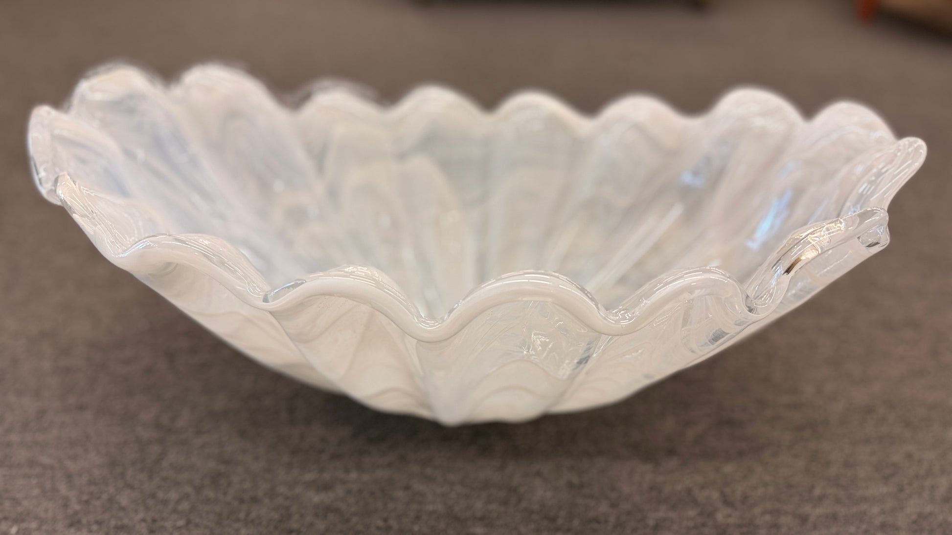 An elegant 20-inch wide decorative glass centerpiece bowl in an opalescent milky-white color, featuring a deeply ruffled and scalloped edge shaped like a sea shell.