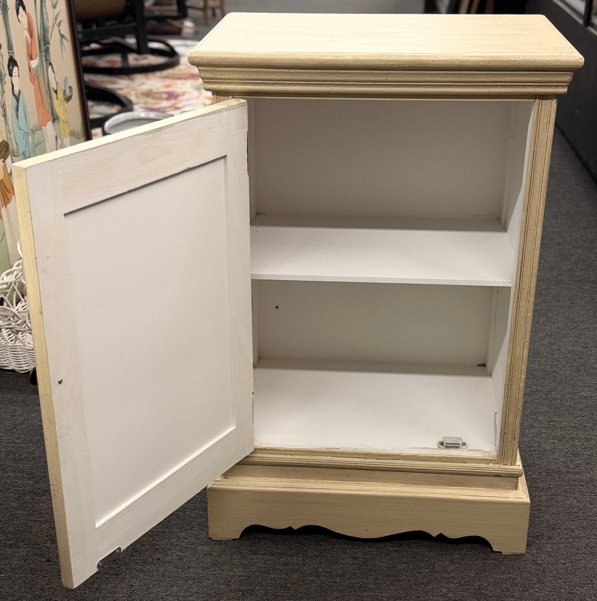 A small rustic accent cabinet with a distressed beige-cream painted finish, featuring a single louvered shutter door with a small dark round knob.