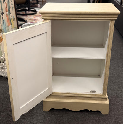 A small rustic accent cabinet with a distressed beige-cream painted finish, featuring a single louvered shutter door with a small dark round knob.