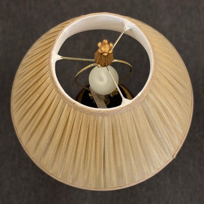 A traditional-style table lamp featuring an urn-shaped ceramic base with decorative gold-toned bands at the neck and base, topped with a pleated flared fabric lampshade.