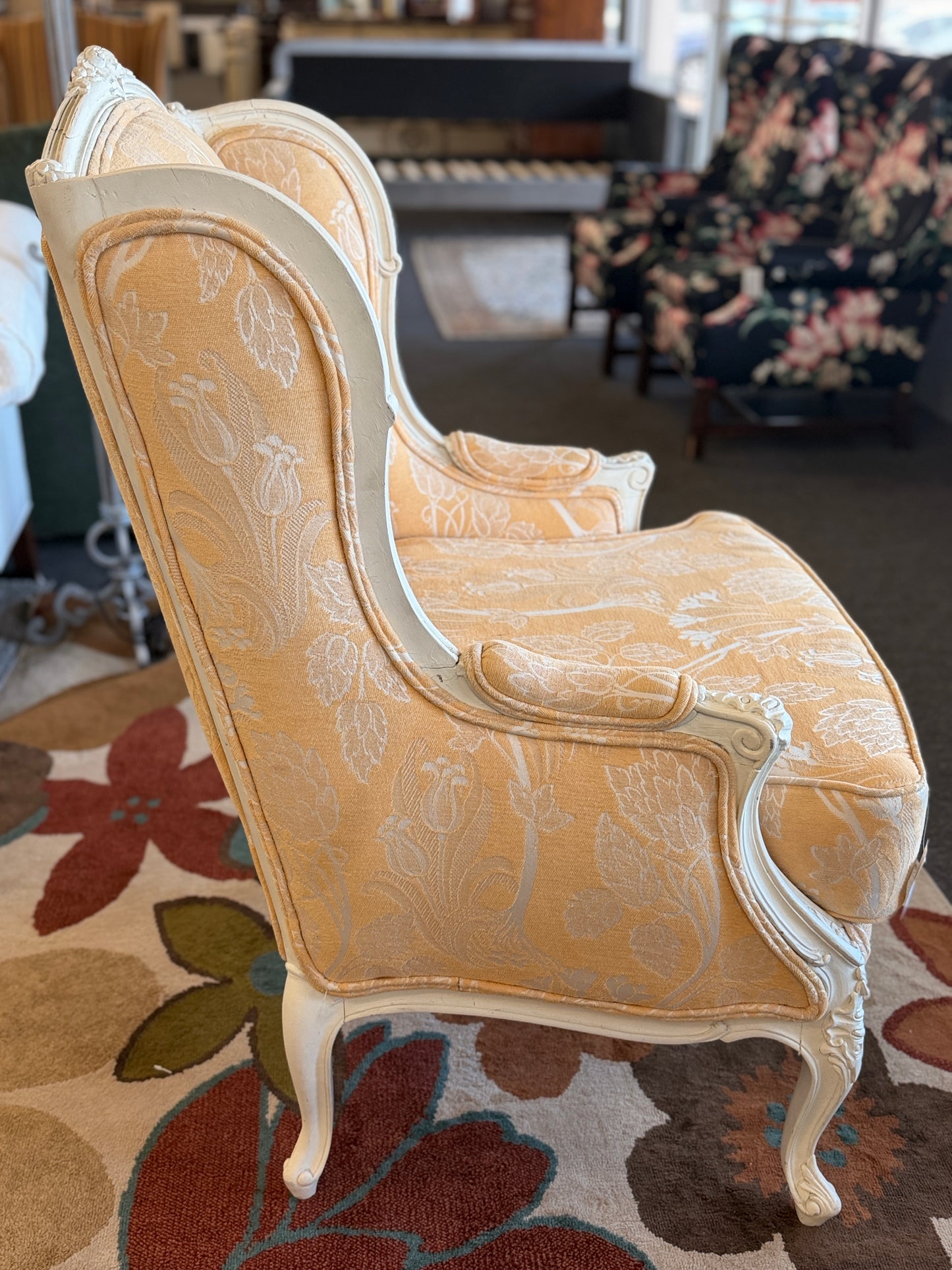 An elegant French provincial-style wingback armchair with an ornate carved white wood frame, tufted-style high backrest, loose seat cushion, and curved cabriole legs.