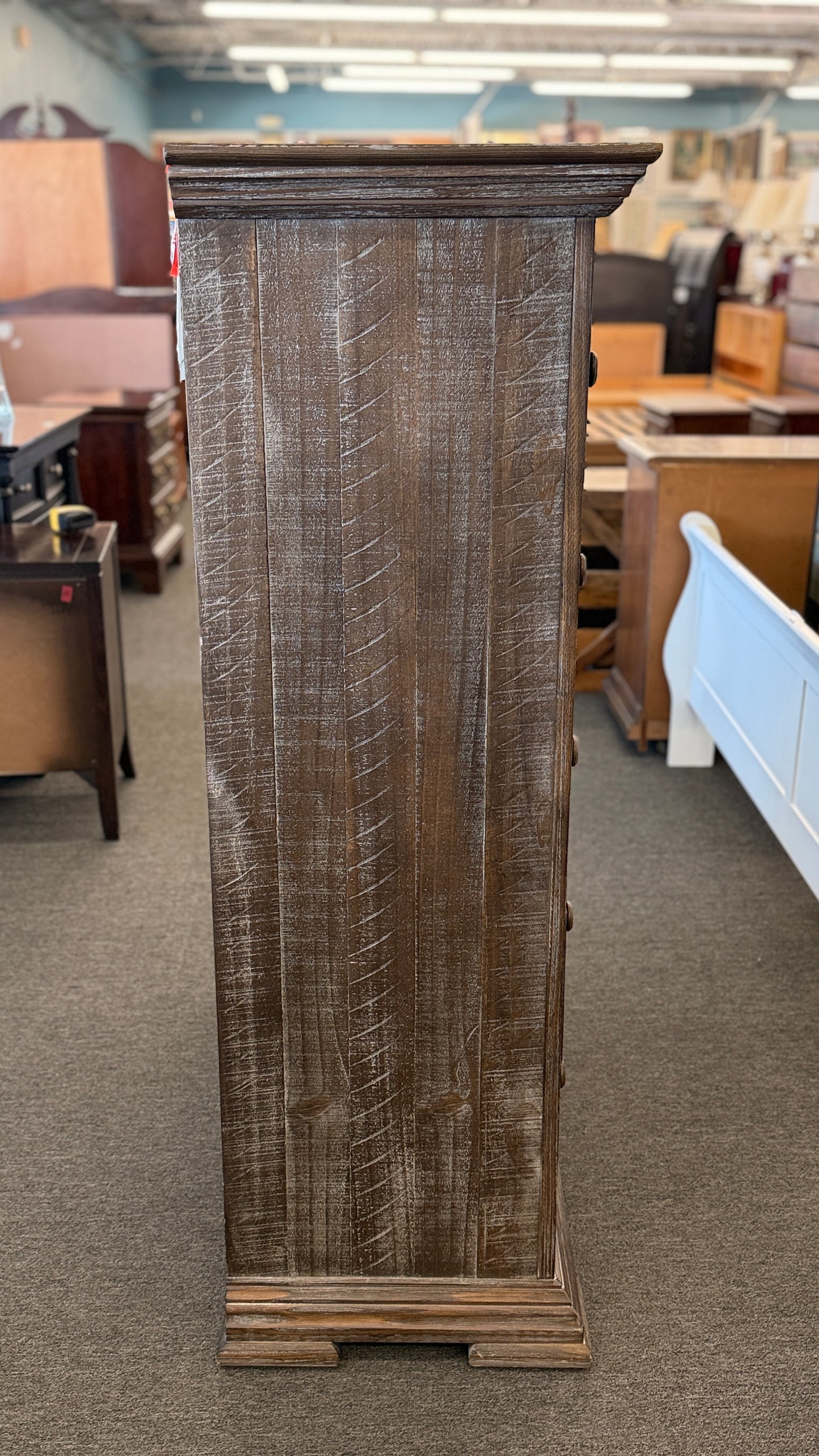 A tall rustic 5-drawer chest of drawers featuring a weathered white-washed finish over dark wood, a crown-molding top, and pairs of round matching knobs.