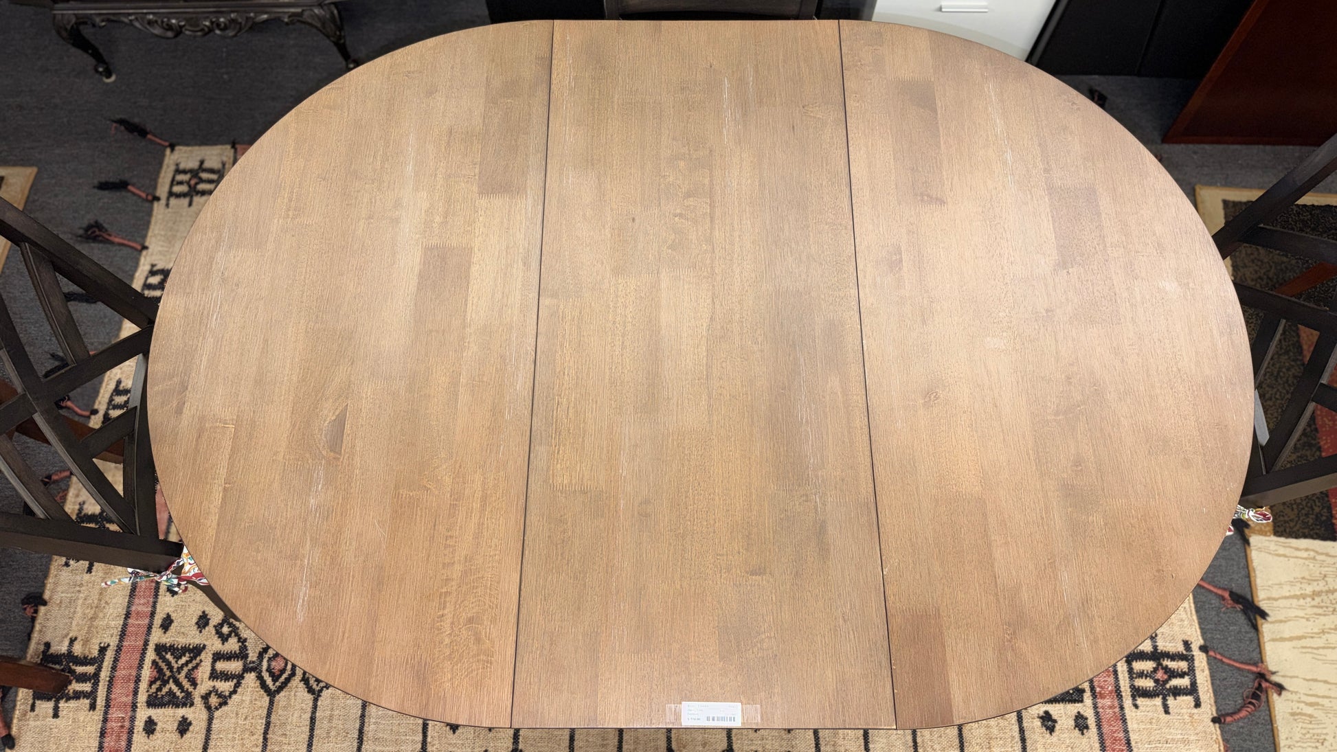 A casual oval dining table set featuring a mid-tone wood top, a dark base with an extendable leaf, and four matching X-back chairs with vibrant paisley-patterned tie-on cushions.