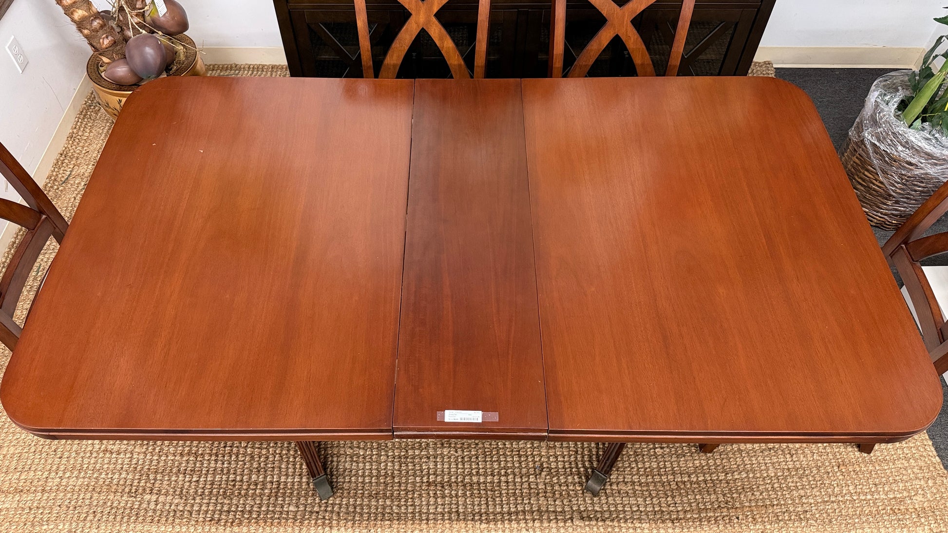 A traditional rectangular wooden dining table with an extendable leaf, twin turned pedestal bases, and six matching X-back dining chairs with light padded seats.