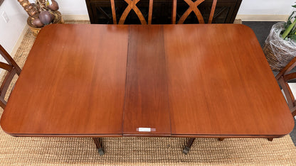 A traditional rectangular wooden dining table with an extendable leaf, twin turned pedestal bases, and six matching X-back dining chairs with light padded seats.