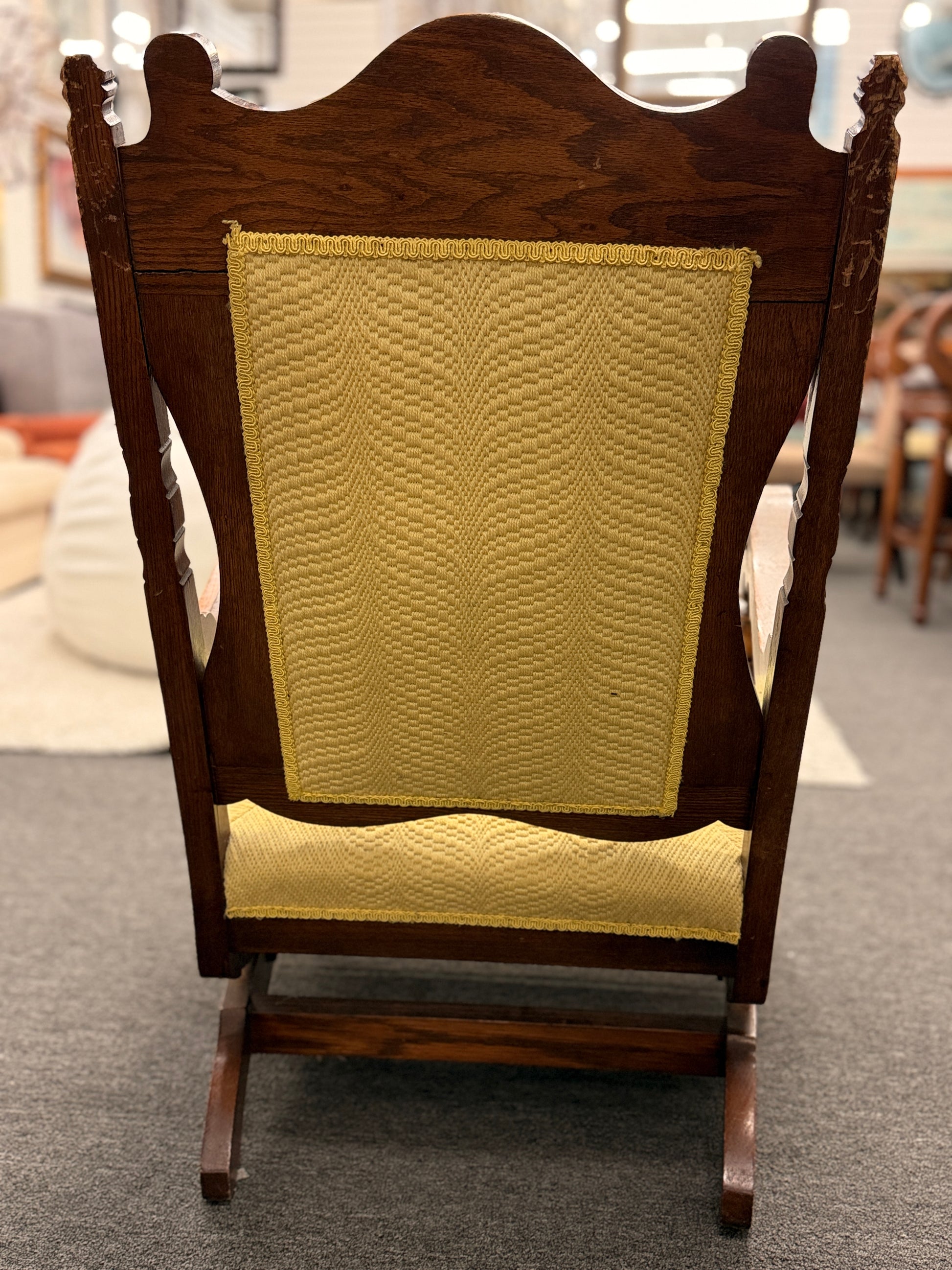 A vintage-style wooden platform rocking chair with an ornate carved crest rail, custom yellow upholstery, and a geometric green and blue embroidered center design.